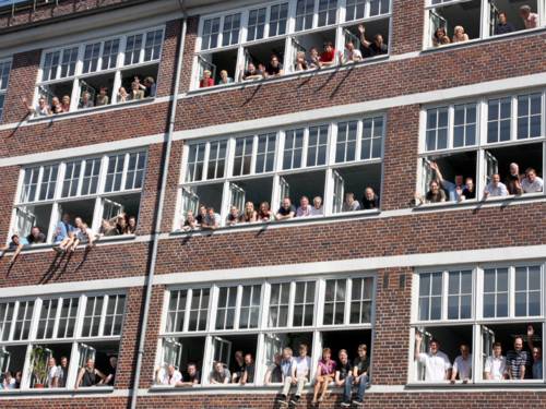 Viele Menschen schauen in einer Häuserfront aus den Fenstern.