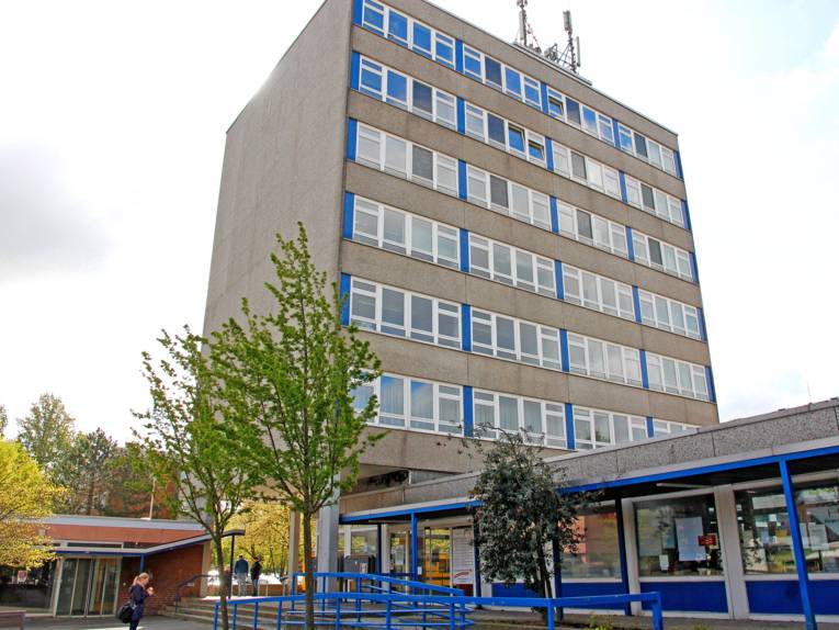 Vor einem siebenstöckigem Gebäude am Bemeroder Rathausplatz ist ein ebenerdiger Anbau mit dem Bürgeramt Bemerode zu sehen, der über eine Rampe und eine Treppe zu erreichen ist.