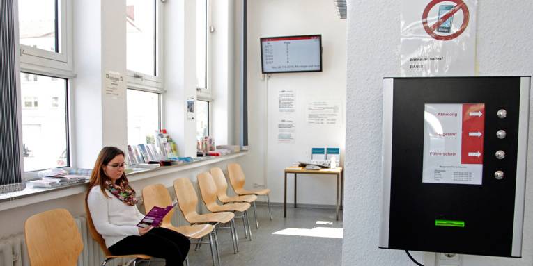 Im Wartebereich des Bürgeramtes Herrenhausen liest eine junge Frau in einer Broschüre, während die elektronische Anzeige Auskunft über die Bearbeitungsplätze gibt.